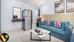 A modern living room with a blue sofa, a white coffee table, and a refrigerator.