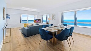 A modern living room with a dining area, large windows, and a view of the ocean. - Ocean View 2BR Condo w/ Pool and Resort Access (Miami)
