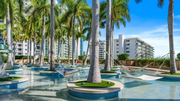 A resort with multiple swimming pools, palm trees, and a modern building in the background. - Ocean View 2BR Condo w/ Pool and Resort Access (Miami)