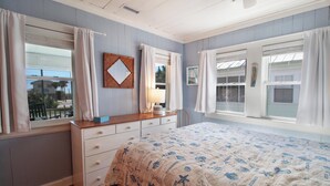 Un dormitorio con cama, cómoda y dos ventanas con cortinas.