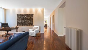 A spacious room with a wooden floor, a white armchair, a blue sofa, a patterned tapestry, and a radiator. - A Casa Di Camillo, Nepi, a C (Nepi)