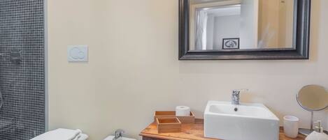 A bathroom with a toilet, bidet, sink, mirror, and a wooden vanity.