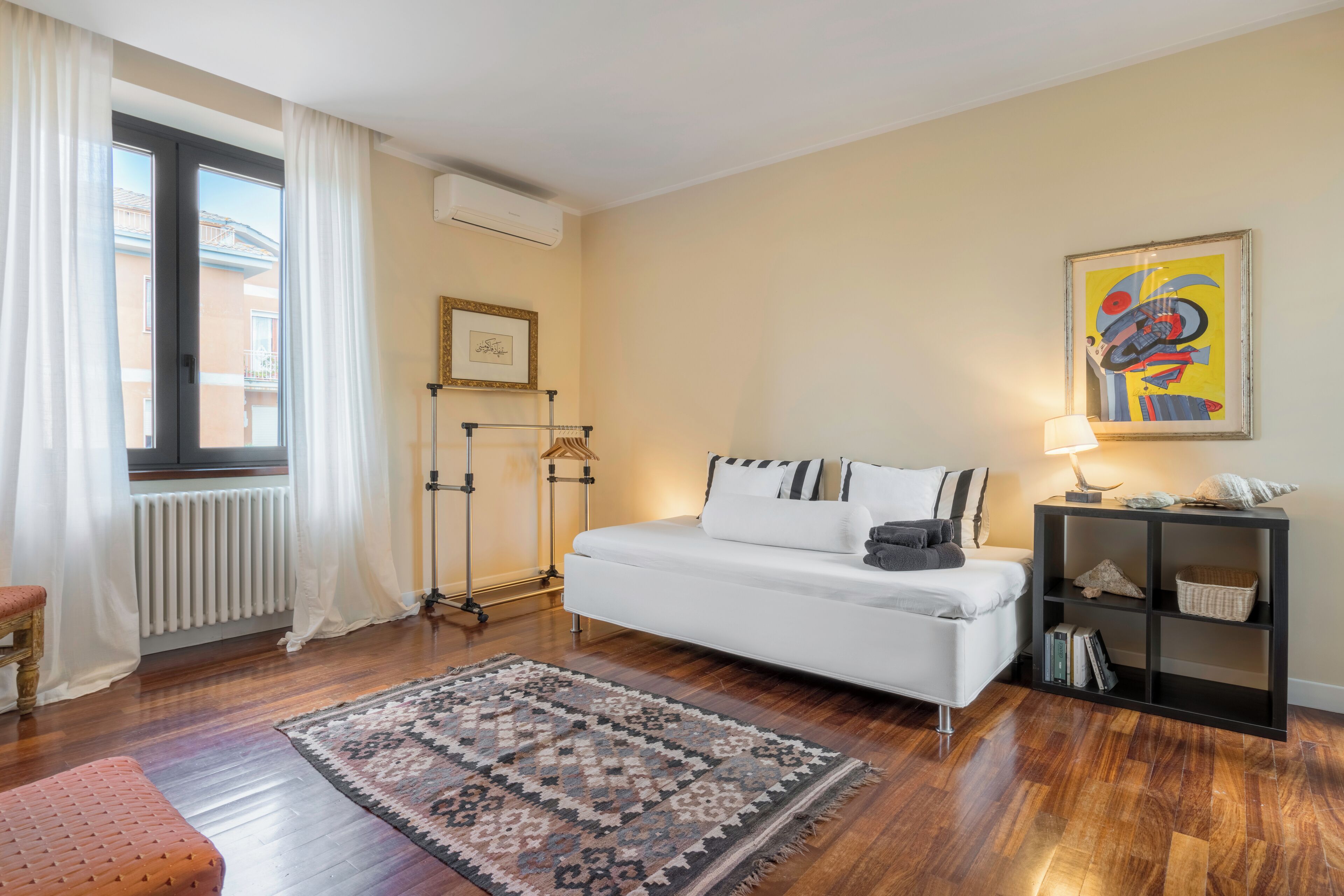 A modern living room with a white sofa, a patterned rug, a side table with books, and a colorful abstract painting on the wall.