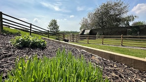 Ländliche Landschaft mit Steinmauer, Holzpforte und grüner Vegetation.