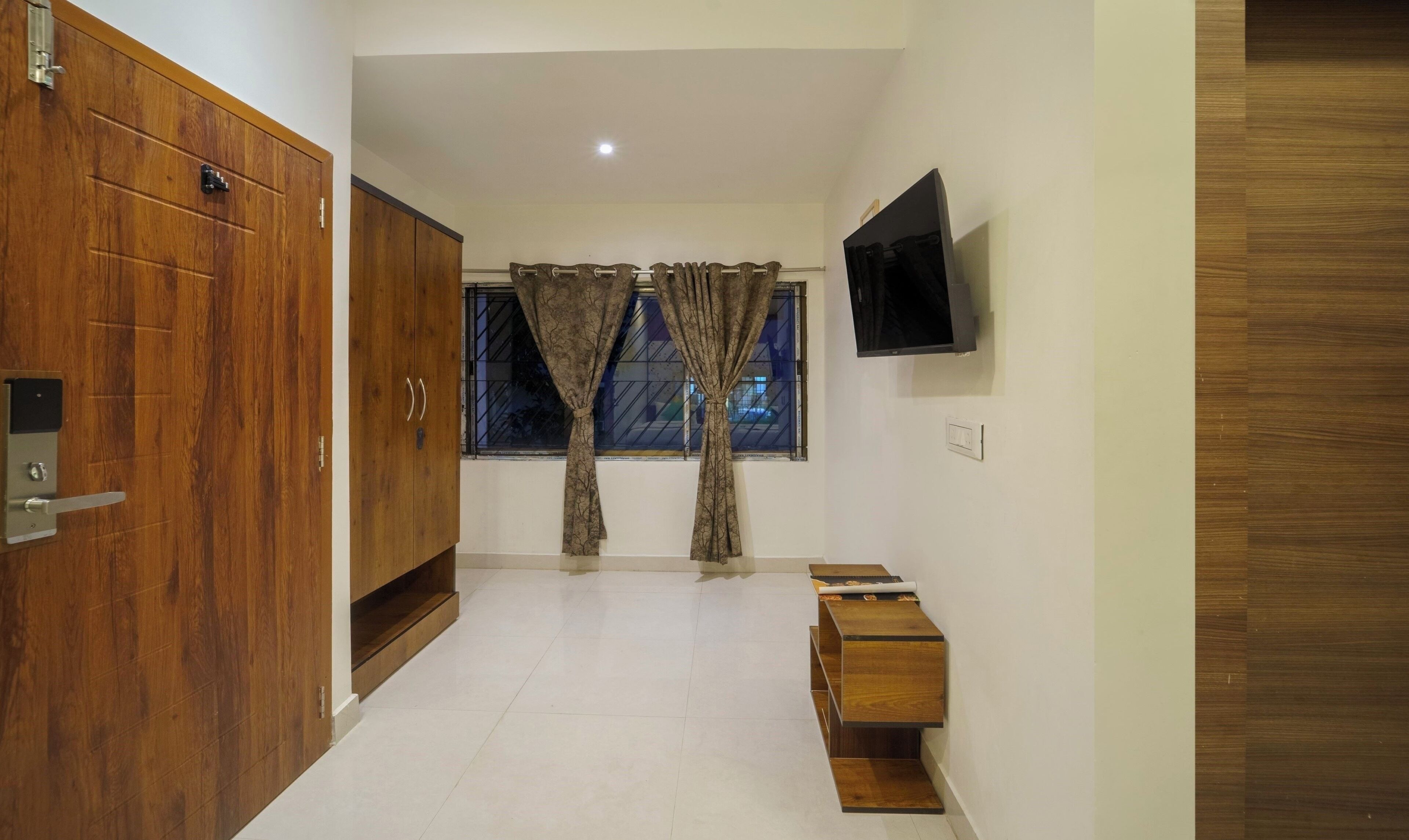 A hallway with a wooden wardrobe, a television mounted on the wall, and a window with curtains.