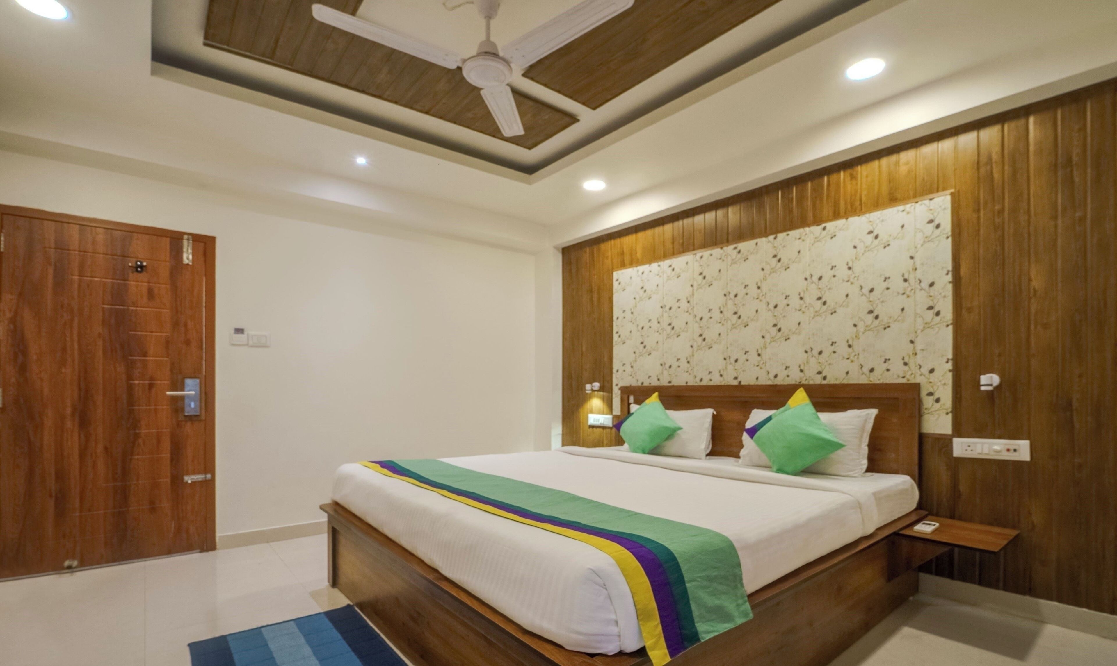 A bedroom with a wooden headboard, a bed with a colorful blanket, a ceiling fan, and a wooden door.