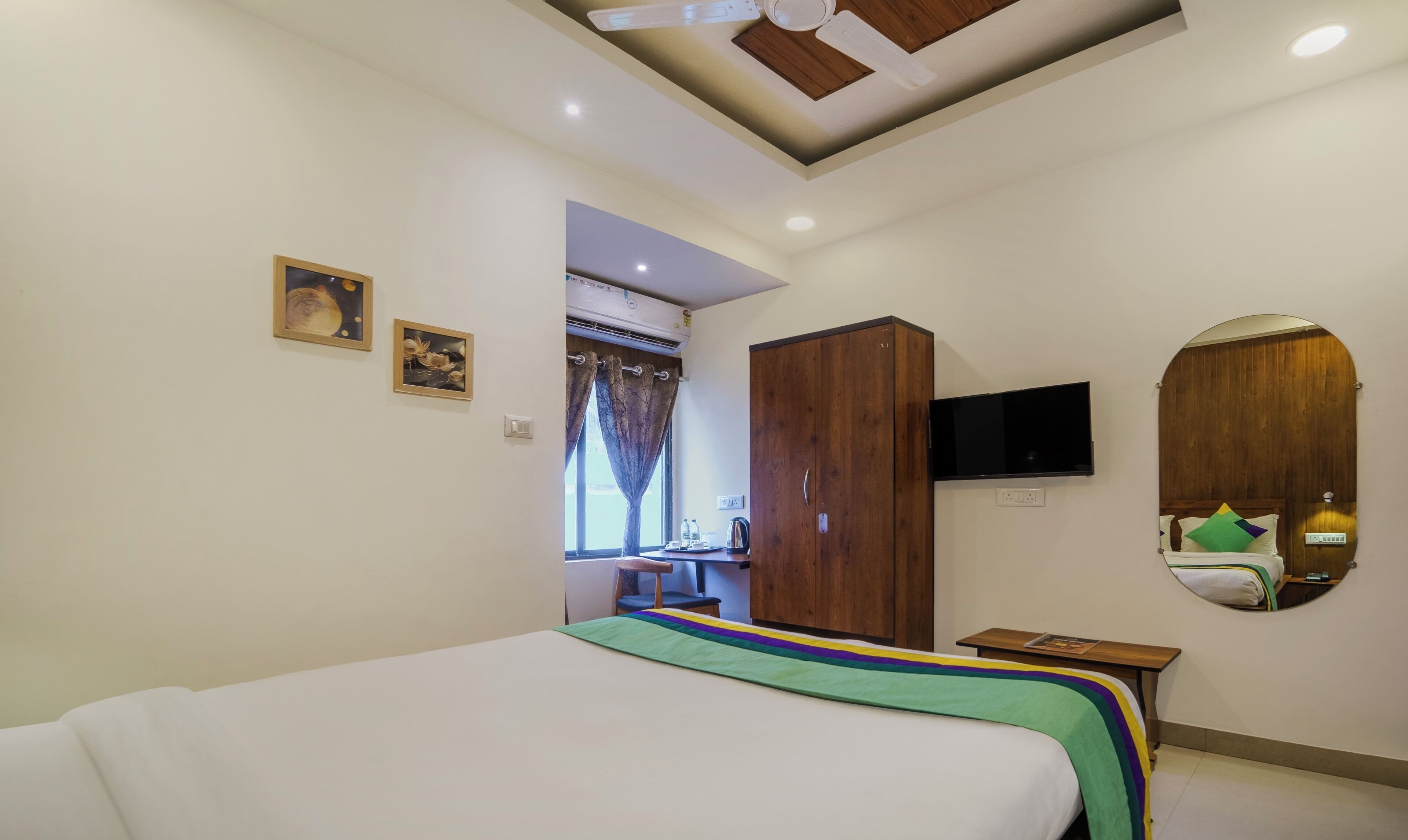 Een hotelkamer met een bed, een aan de muur bevestigde televisie, een kledingkast en een klein tafeltje met een waterkoker.