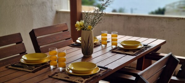 A wooden dining table set with yellow plates, glasses, and a vase with flowers.