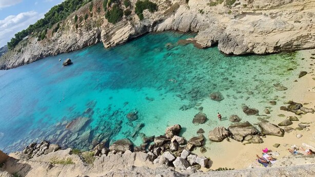 Un paisaje costero con aguas turquesas cristalinas, acantilados rocosos y una playa de arena.