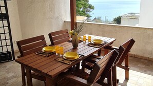 Una mesa de madera con sillas y platos amarillos, sobre un suelo de baldosas bajo un techo con vigas de madera.