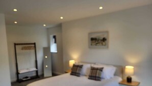 A bedroom with a bed, bedside lamps, a nightstand, a mirror, and a painting on the wall.