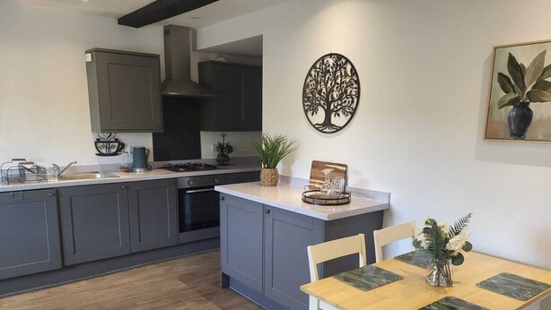 A modern kitchen with grey cabinets, a central island, and a dining area with a wooden table and chairs.