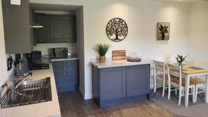 A modern kitchen with grey cabinets, a wooden dining table, and a decorative tree wall art piece.