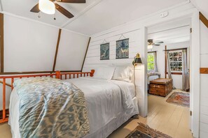 Quarto com cama, ventoinha no teto, mesa de cabeceira, abajur e janela com cortinas.