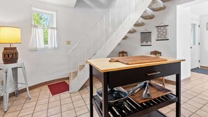 Una cocina moderna con una mesa de madera, un colgador de ollas y una escalera con detalles de piedra.