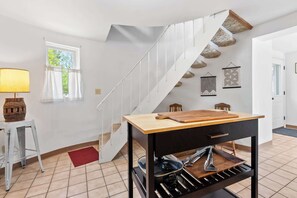 A modern kitchen with a wooden table, a hanging pot rack, and a staircase with stone accents.