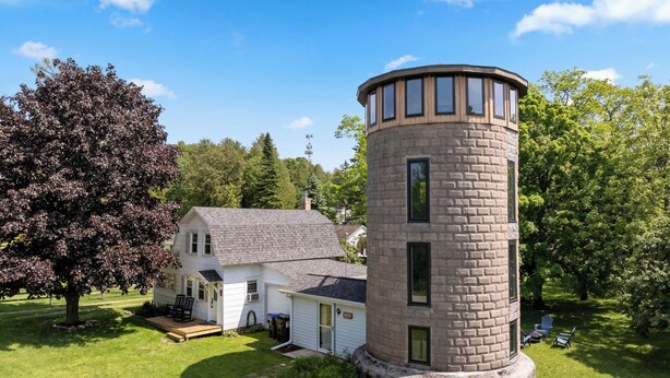 Una casa blanca con techo gris, una torre de piedra y un árbol en primer plano.