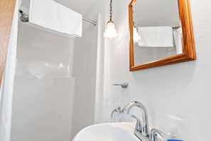 Une salle de bain avec un lavabo blanc, un miroir et une douche.