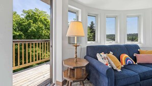 Una habitación con un sofá azul, una mesita de madera con una lámpara y vistas a zonas verdes a través de amplias ventanas.
