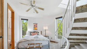 Un dormitorio con cama, mesita de noche, lámpara, ventilador de techo y una escalera.