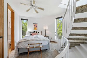 A bedroom with a bed, a bedside table, a lamp, a ceiling fan, and a staircase.