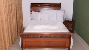 A neatly made bed with white linens and a fluffy white pillow, a wooden nightstand with a telephone, and a green wall in a hotel room. - Hotel Business (Bogotá)