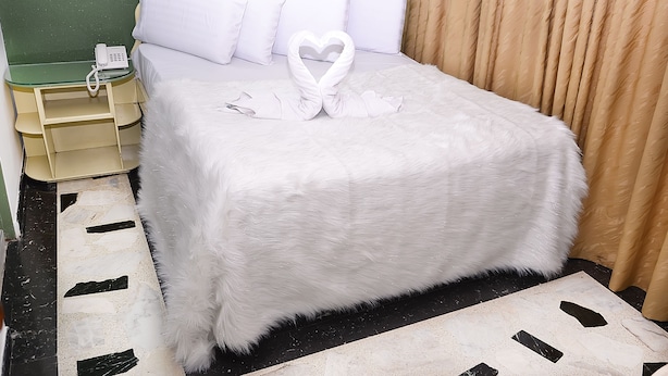 A neatly made bed with white linens and a heart-shaped towel arrangement. - Hotel Business (Bogotá)