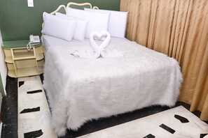 A neatly made bed with white linens and a heart-shaped towel arrangement. - Hotel Business (Bogotá)