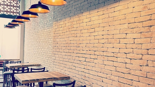 Interior de restaurante con paredes de ladrillo, mesas de madera y lámparas colgantes.