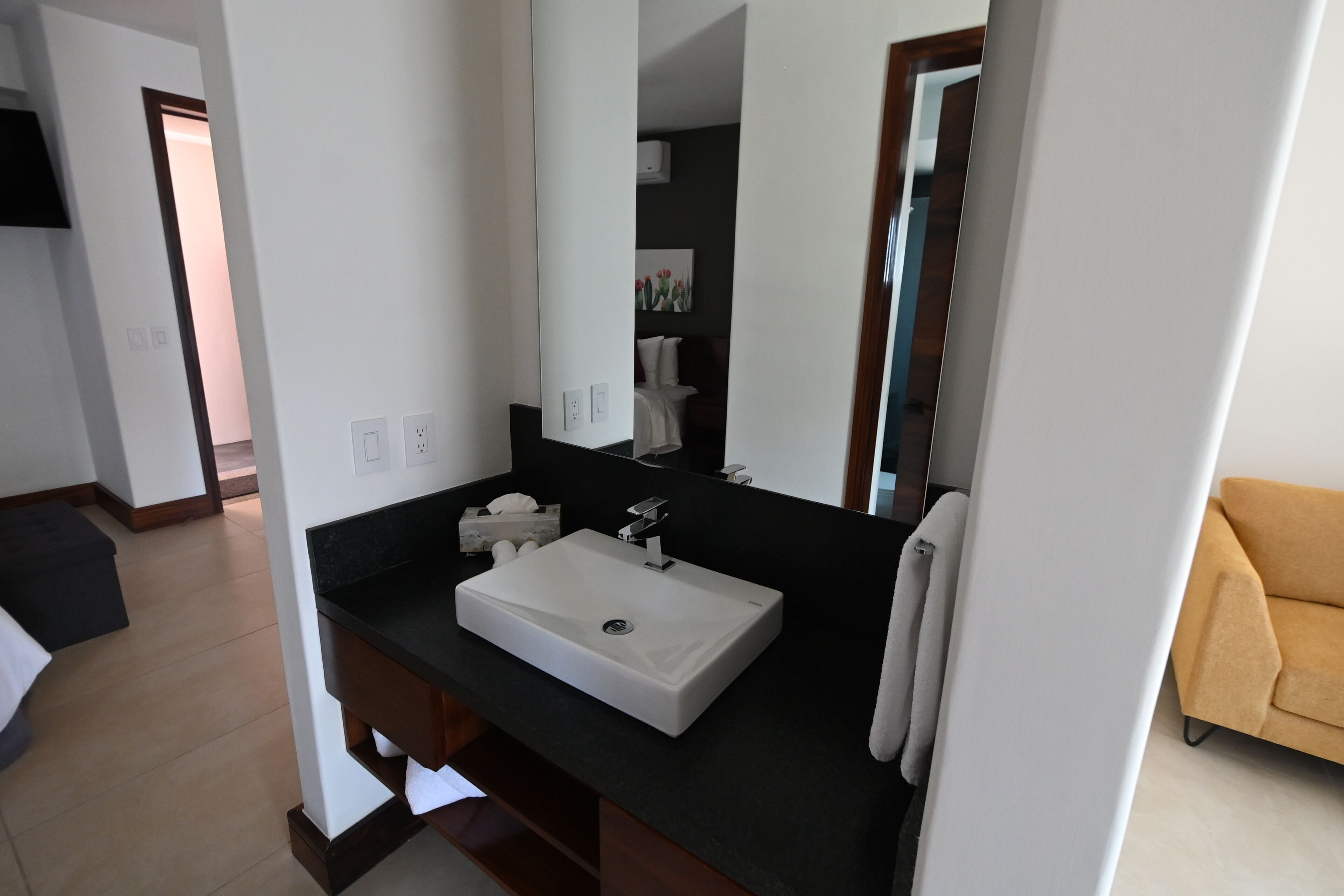 Une salle de bain moderne avec un lavabo blanc, un plan de toilette foncé et un grand miroir.
