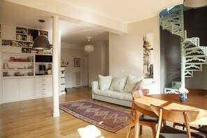 A living room with a sofa, wooden dining table, and a spiral staircase. - Beautiful Family apt With Terrace (Paris)