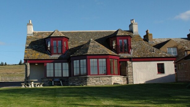 A large, two-story stone house with red-framed windows and a stone roof.