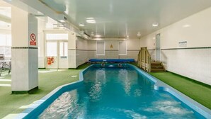 An indoor swimming pool with clear water, tiled walls, and a staircase leading to an upper level.