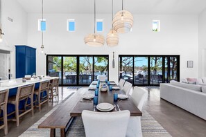A spacious dining area with a long wooden table set for a meal, surrounded by white chairs.