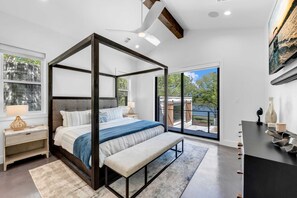 Ein modernes Schlafzimmer mit einem Himmelbett, einer Sitzbank, einem Nachttisch und einem großen Fenster mit Blick ins Freie.