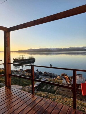A wooden deck with a view of a calm lake and mountains in the distance. - Los Dones Departamentos DAT (San Carlos de Bariloche)