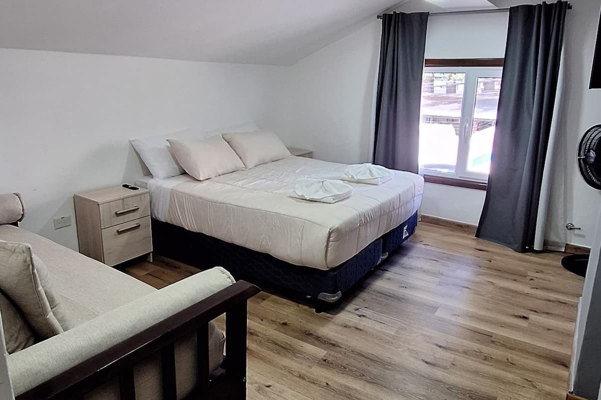 Ein Schlafzimmer mit Bett, Sofa, einem kleinen Tisch und einem Fenster mit Vorhängen.
