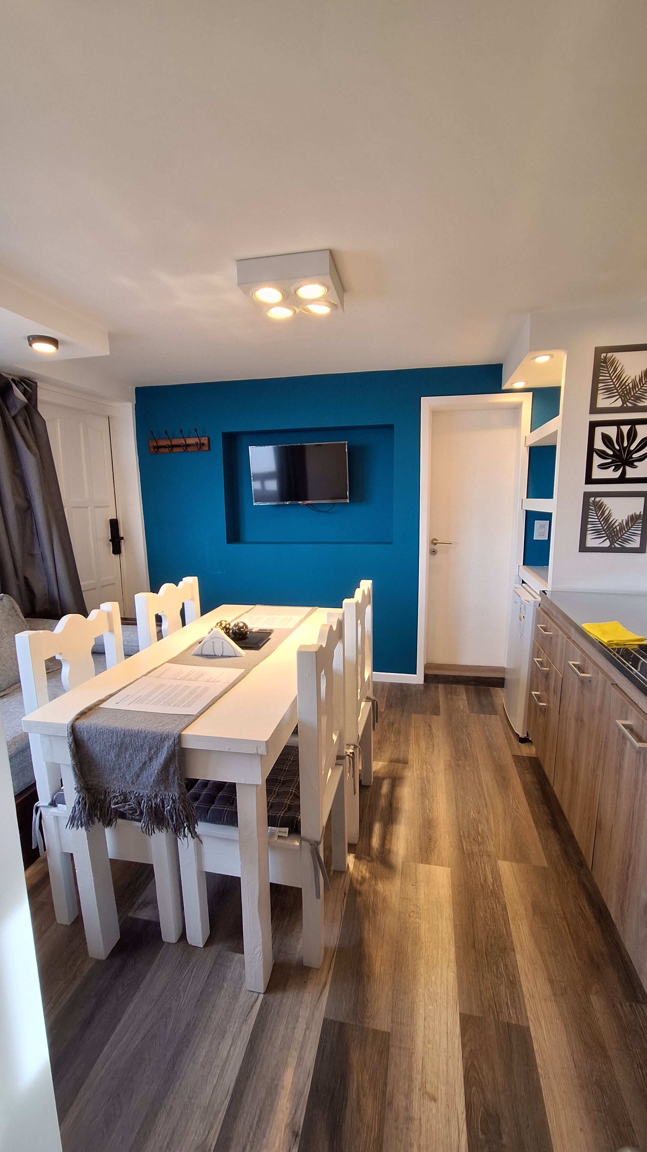 A modern kitchen with white cabinetry, a blue accent wall, and a dining area with a white table and chairs.