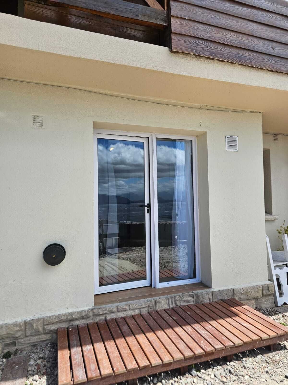 A building with a sliding glass door, a wooden bench outside, and a stone wall.