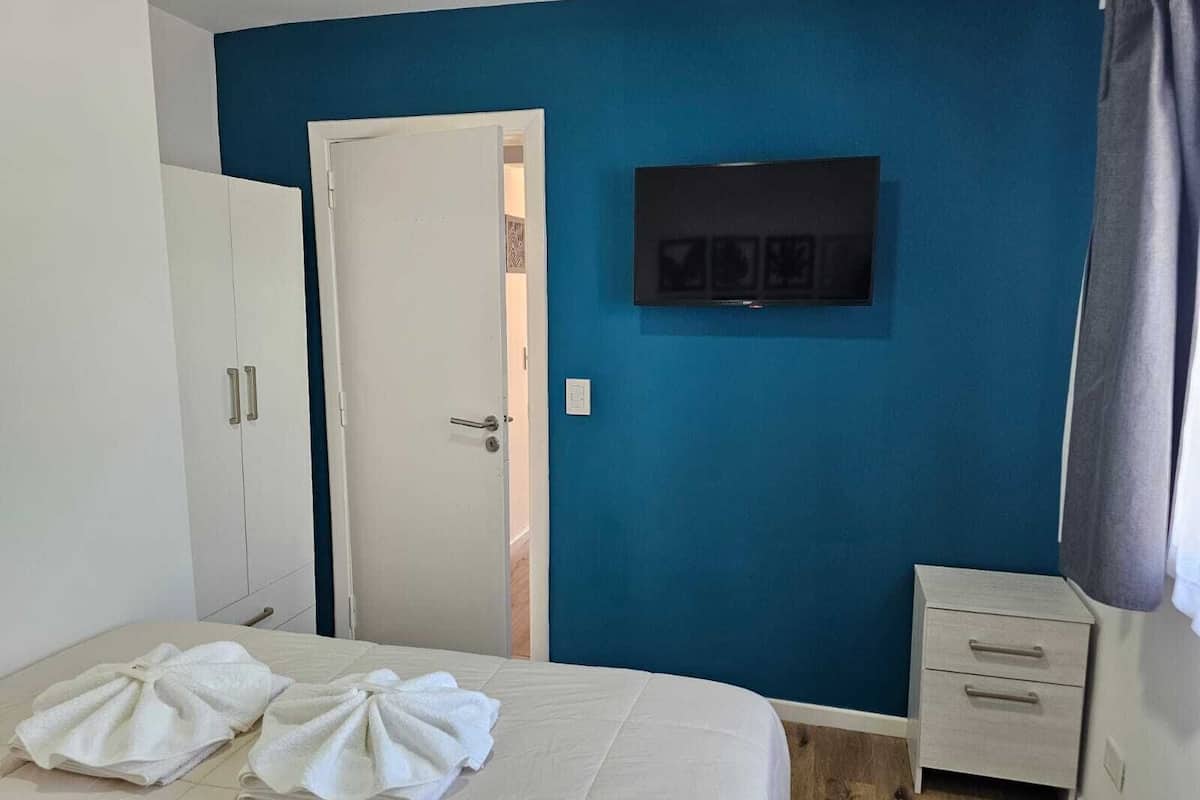 Ein Hotelzimmer mit Bett, Kleiderschrank, Nachttisch und Fernseher an der Wand.