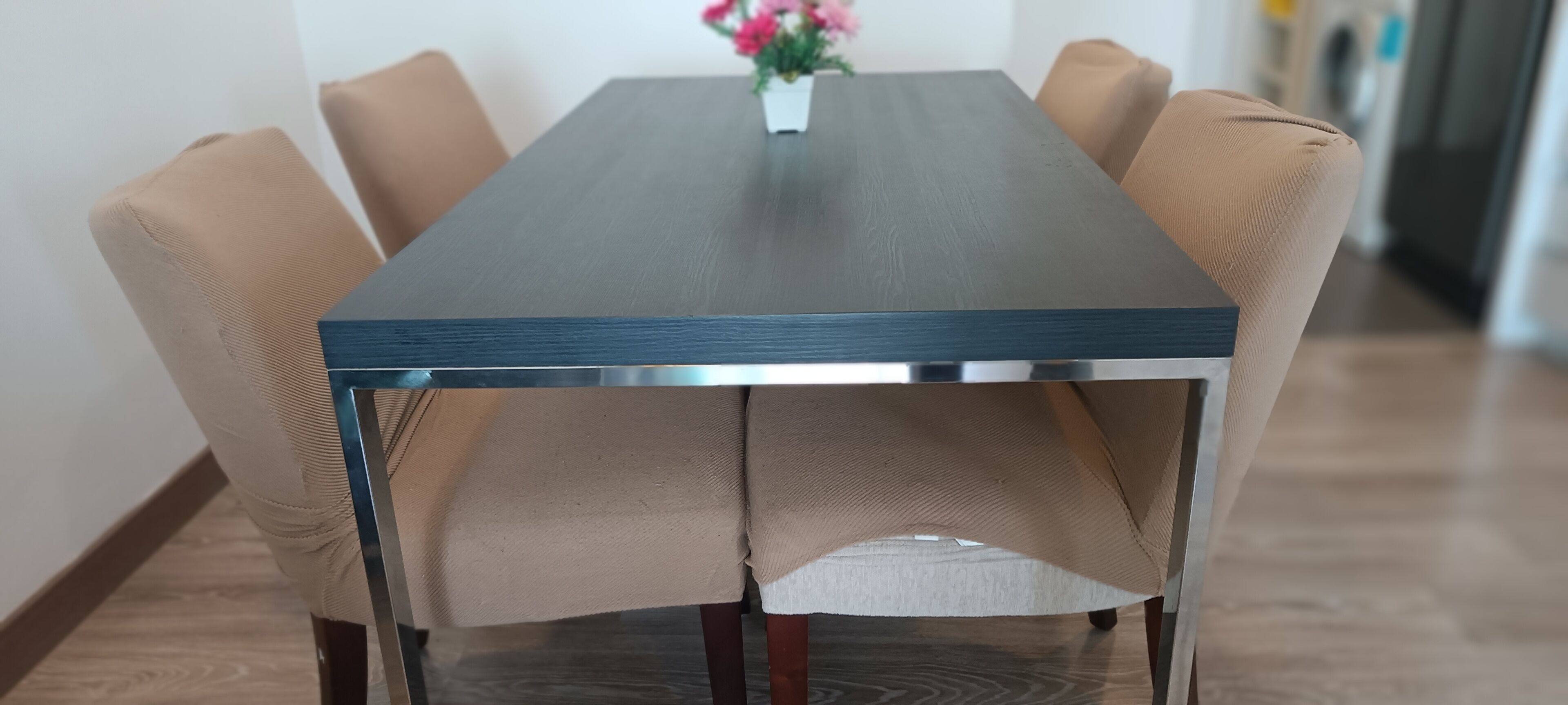 A dining table with a dark wooden top and metal legs, surrounded by beige upholstered chairs.