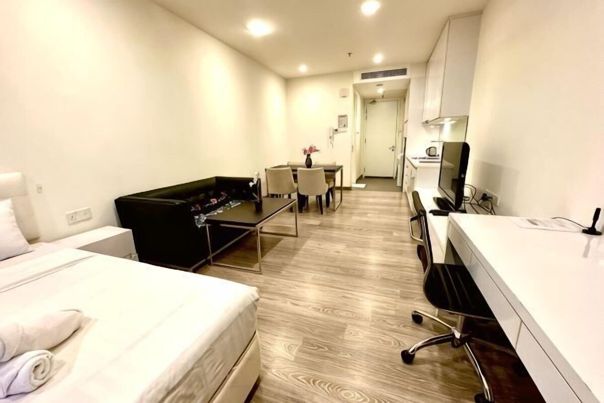 Une chambre d’hôtel avec un lit, un canapé noir, un bureau avec un ordinateur et une petite table avec des chaises.