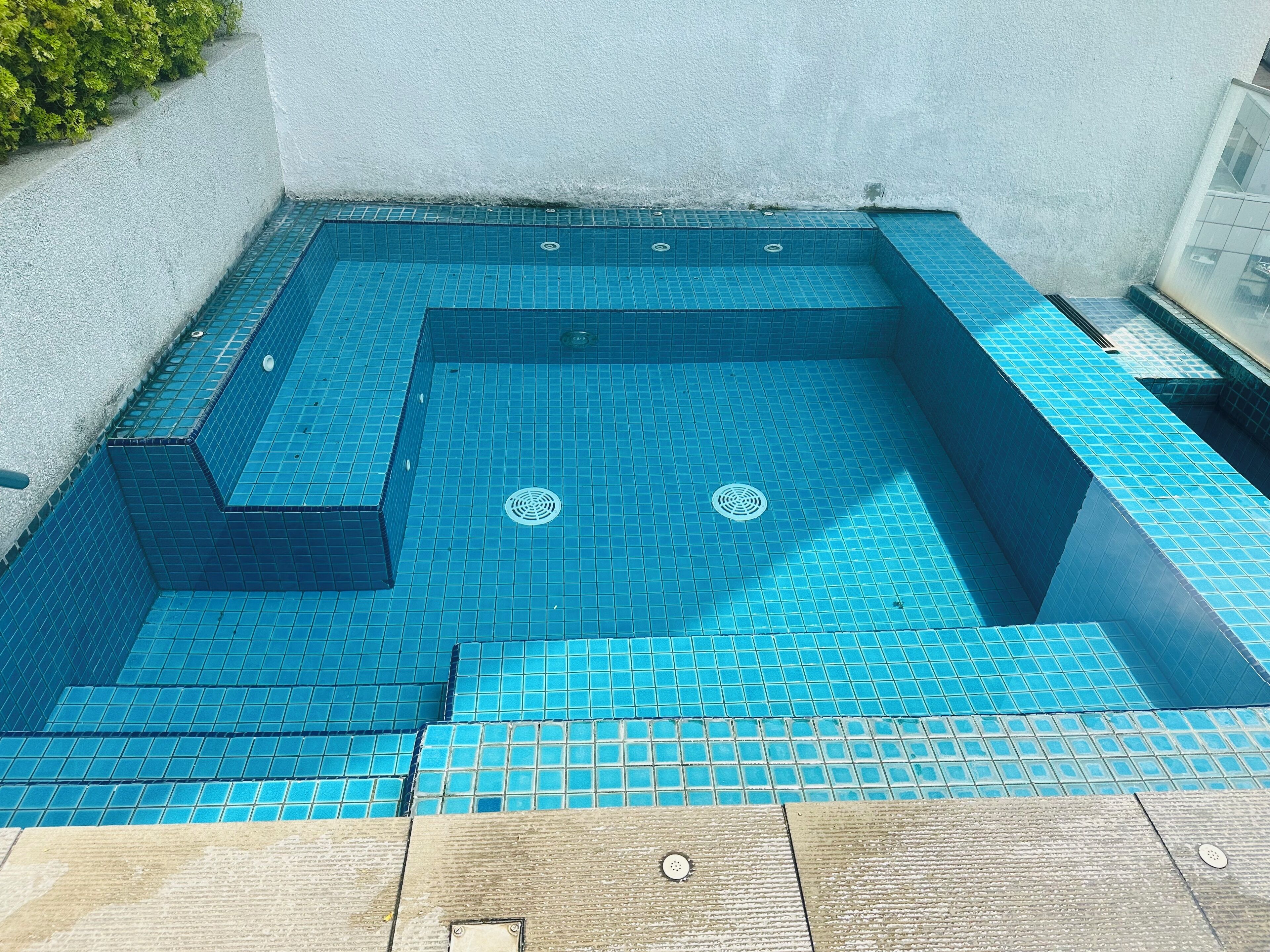 Una piscina pequeña y cuadrada con azulejos azules y un desagüe en el centro.