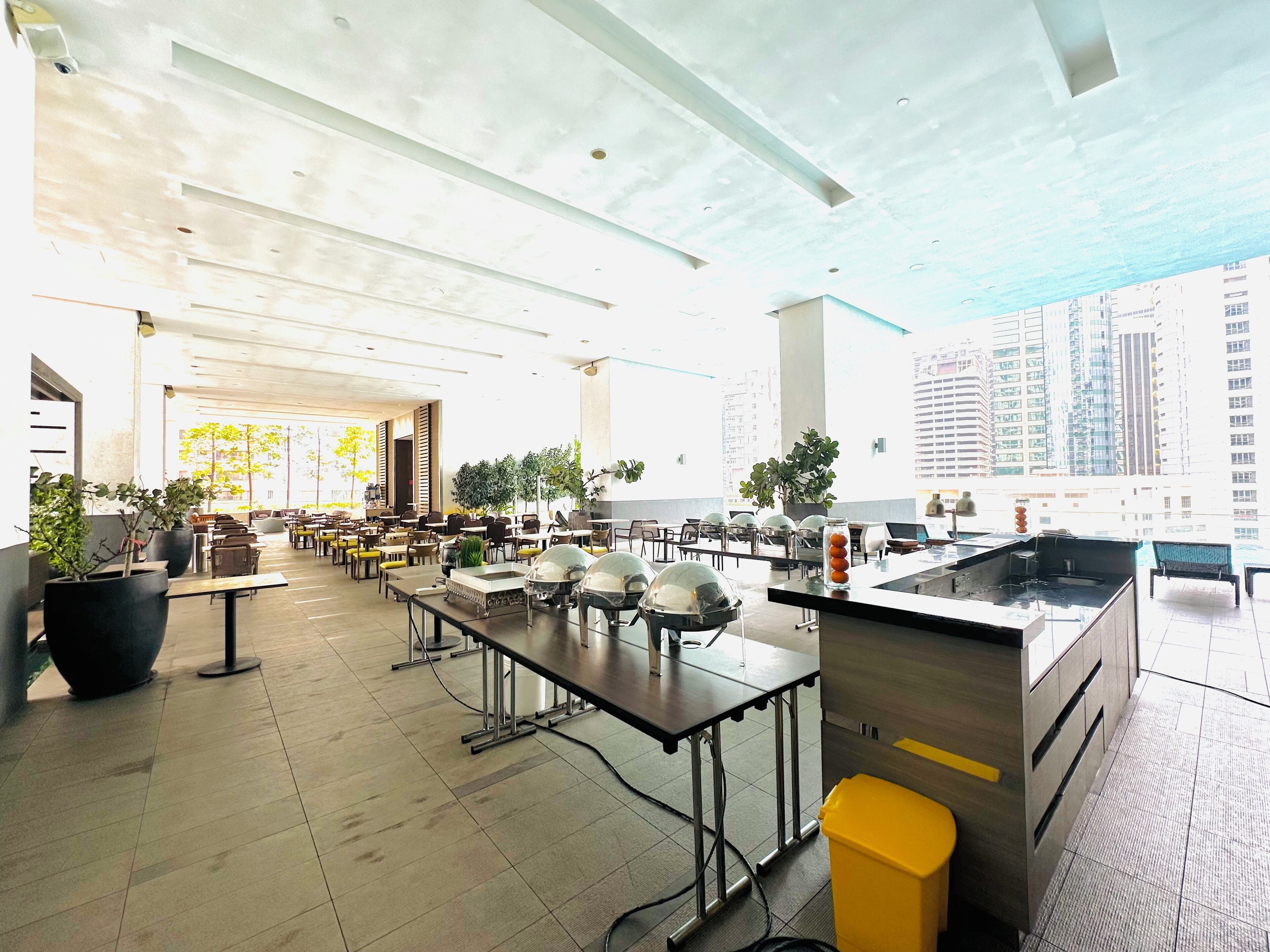 A spacious indoor dining area with high ceilings, multiple tables, and potted plants.
