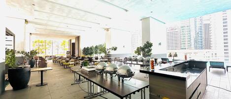 A spacious indoor dining area with high ceilings, multiple tables, and potted plants.