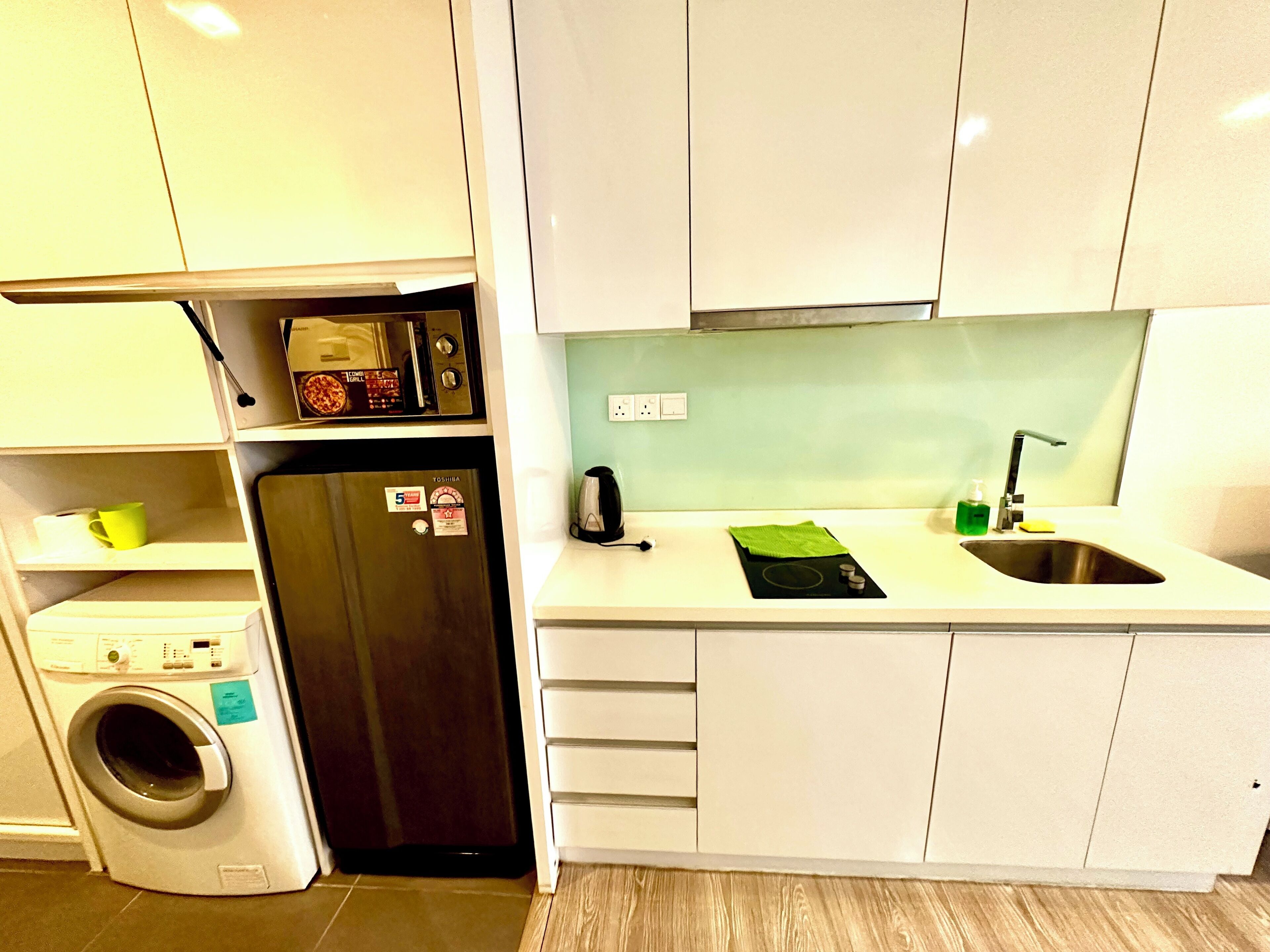 Een kleine keuken met een wasmachine, een magnetron, een spoelbak en een klein aanrecht.