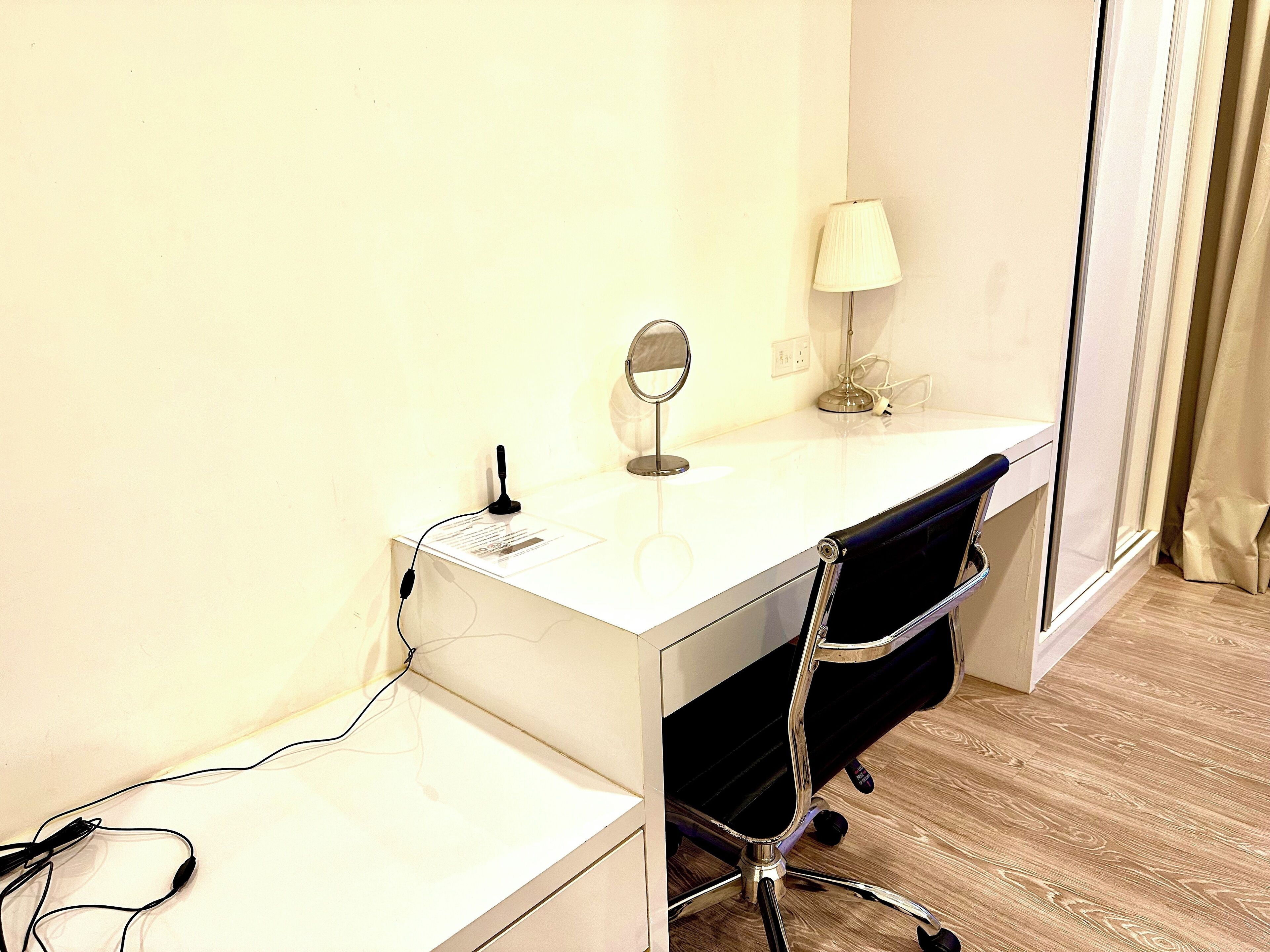 Un escritorio blanco con un espejo, una lámpara y una silla en una habitación con piso de madera.