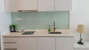 Eine Küche mit weißen Schränken, einer Edelstahl-Spüle, einer grünen Arbeitsplatte, einem schwarzen Kühlschrank, einem kleinen Tisch mit einer Lampe und einigen Küchenutensilien.