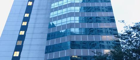 Un edificio alto y moderno con fachada de vidrio reflectante, que presenta una serie de ventanas y balcones.