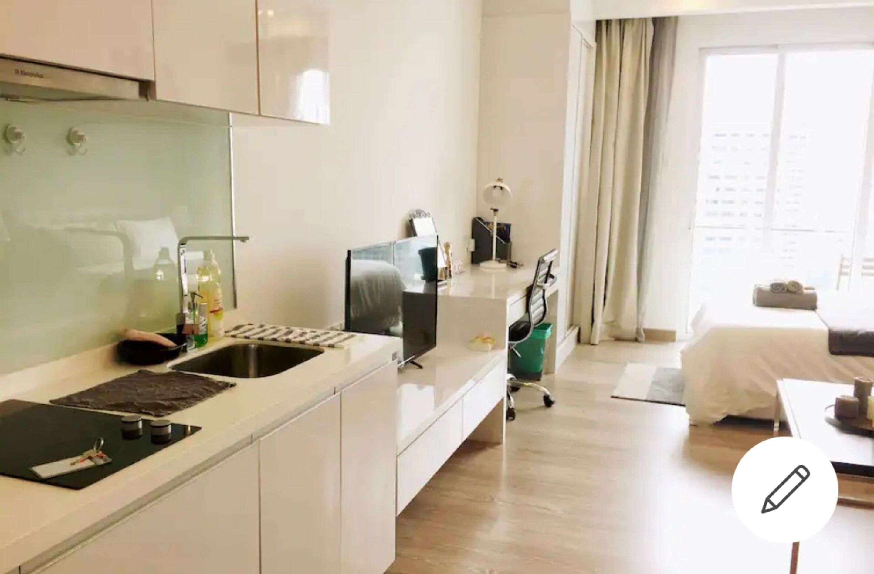 A modern hotel room with a kitchenette, a bed, a desk, and a large window.